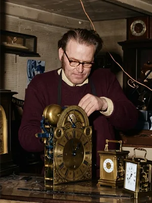 Photograph of Ernest Gordon Roland Lee working meticulously on the intricate internal gears of an antique brass clock.